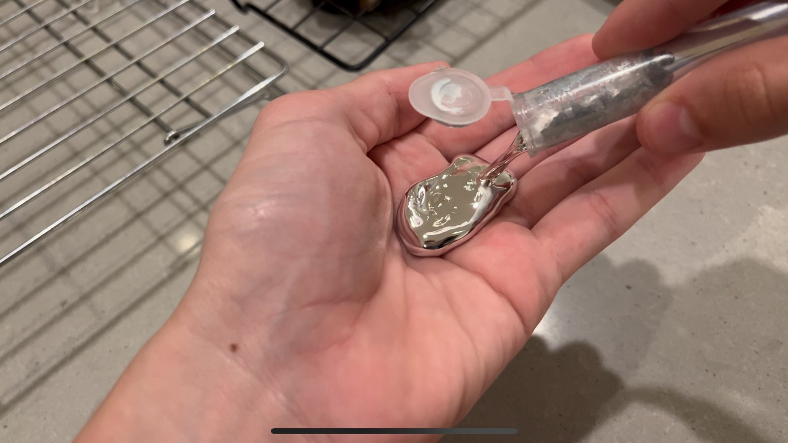 Liquid gallium metal being poured from a syringe into a person's hand, showing its mirror-like liquid metal surface