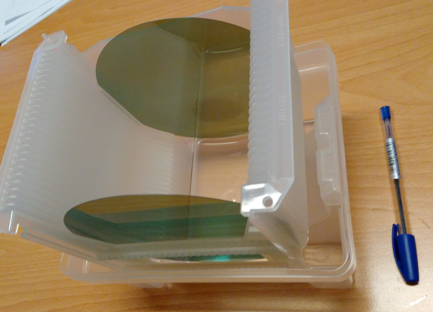 Two six-inch silicon carbide wafers in a plastic transport carrier, next to a ballpoint pen for scale